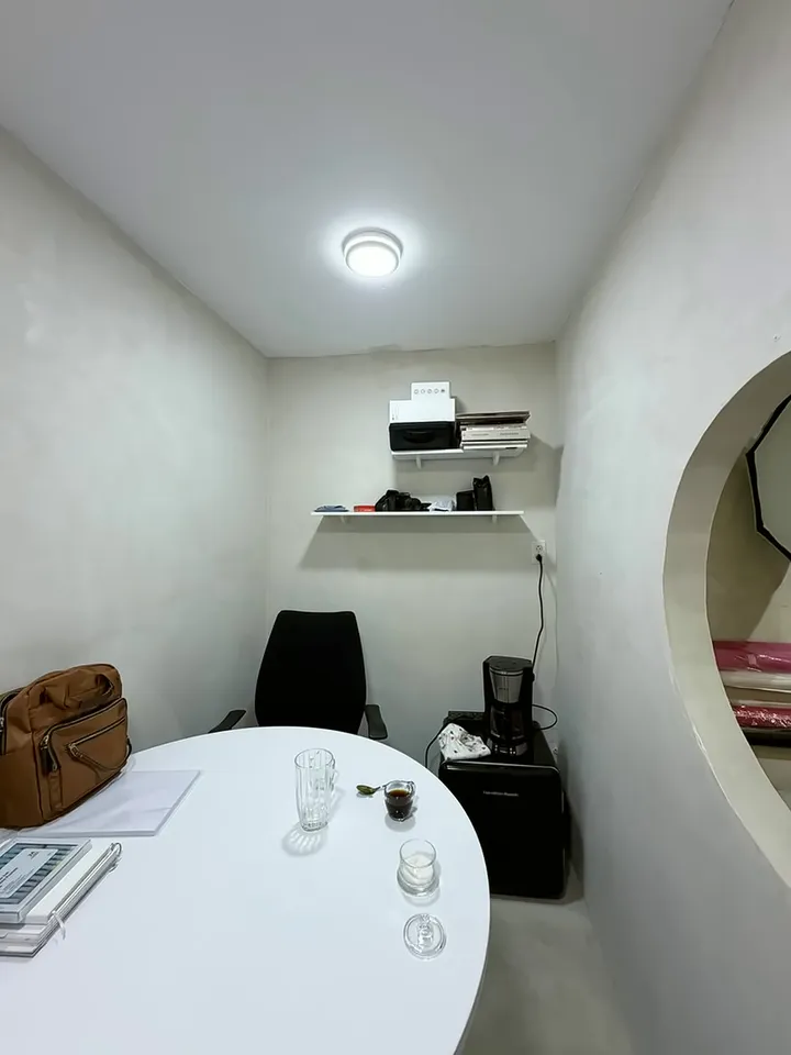 Mesa redonda blanca con una silla y una repisa en un ambiente claro del estudio.
